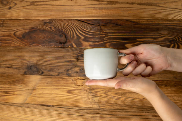 istock Hand Holds Cup, Empty Cup in Hands, Coffee Mug, Teacup Mockup, Cup in Arms on Wooden Table 1838553302