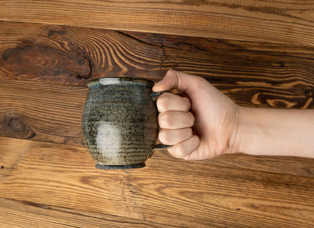 istock Hand Holds Cup, Empty Cup in Hands, Coffee Mug, Teacup Mockup, Cup in Arms on Wooden Table 1838553309