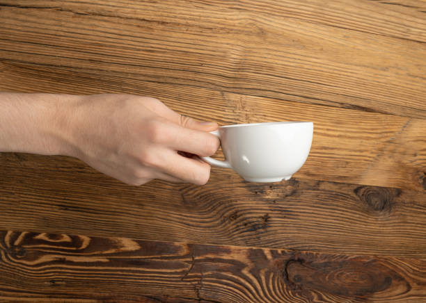 istock Hand Holds Cup, Empty White Cup in Hands, Coffee Mug, Teacup Mockup, Cup in Arms on Wooden Table 1838553322