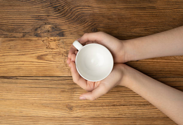 istock Hand Holds Cup, Empty White Cup in Hands, Coffee Mug, Teacup Mockup, Cup in Arms on Wooden Table 1838553828