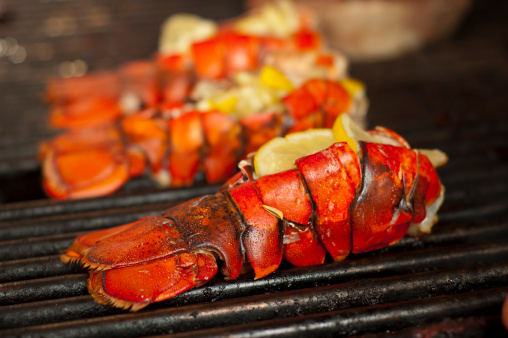 Selective-focus image of lobster tails, stuffed with lemon slices, cooking on a grill