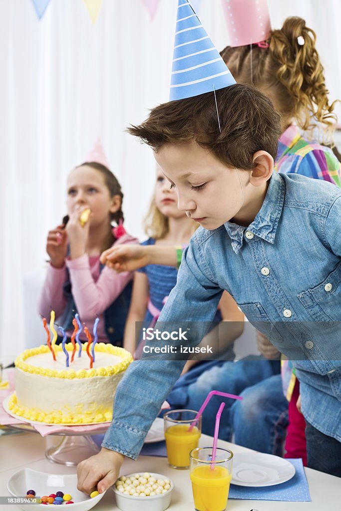 At the birthday party "Kids Birthday Party. Focus on a little boy wearing a party hat taking candies. Kids in the background eating cakes. Vertical shot, selective focus." Birthday Stock Photo