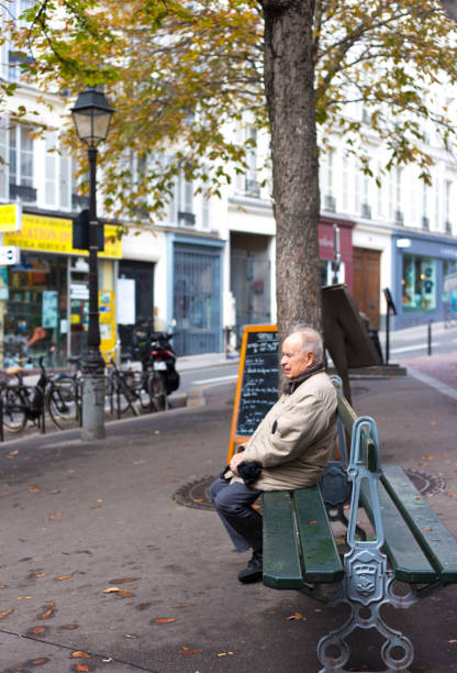 Paris, France: A senior man relaxes on a bench outside under a yellowing autumn tree in the 9th arrondissement.