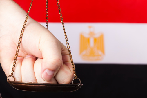 Male hand pressing one part of scale of justice. National flag of Egypt in the background.