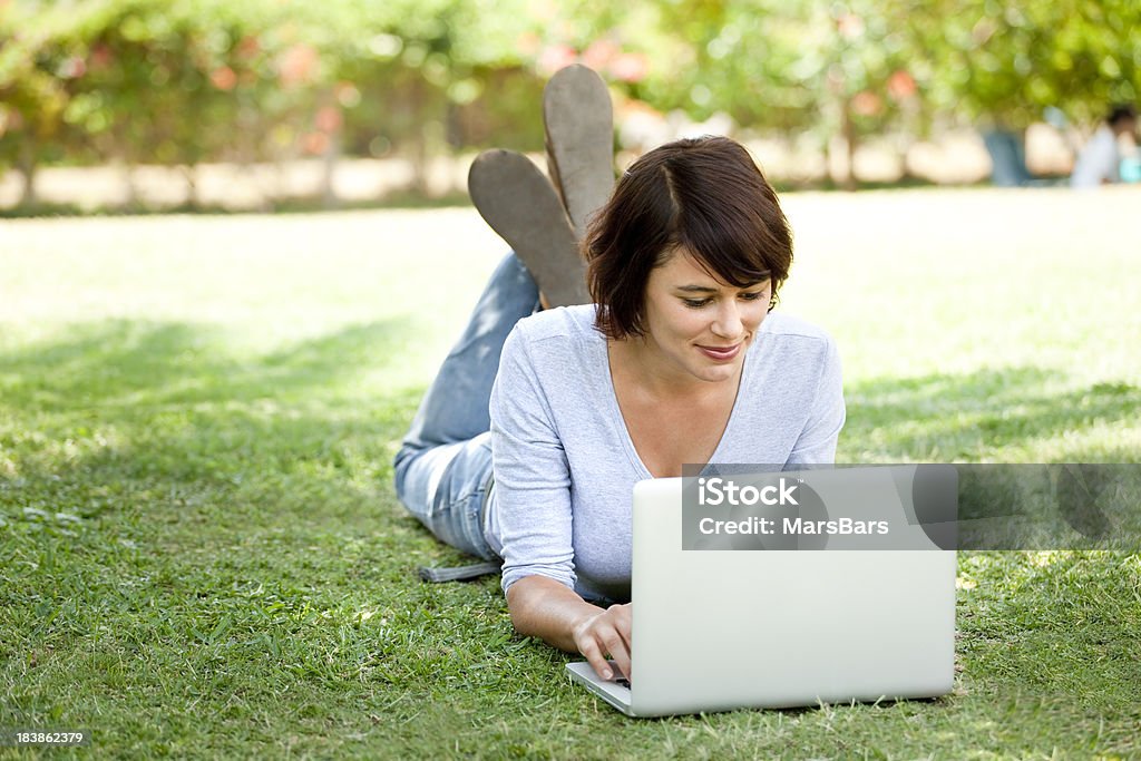 Hermosa mujer joven usando una computadora portátil, lying on grass - Foto de stock de 16-17 años libre de derechos