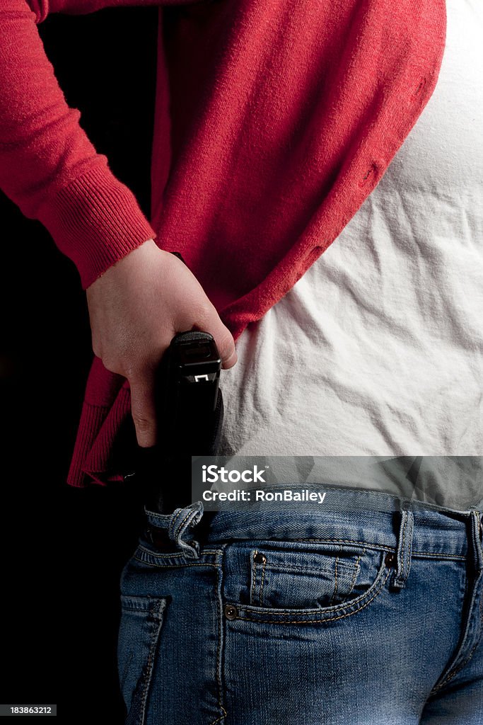 Yound Woman Drawing From an Inside-the-Waistband Holster A young woman drawing her modern polimer pistol from an IWB (inside the waistband) holster under her sweater.All images in this series... Adult Stock Photo