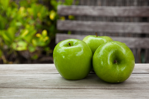 Three organic green apples on an old wood table outdoors