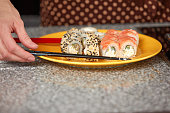 Sushi nigiri with salmon on yellow plate and female hand with chopsticks