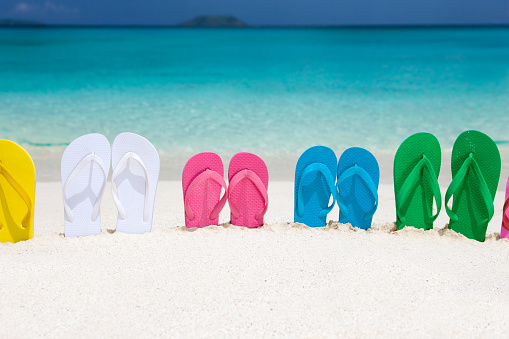 Stylish rainbow flip flops in sand on beach