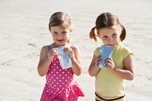 Two little girls, 3 and 4 years, having refreshment on hot summer day at the beach