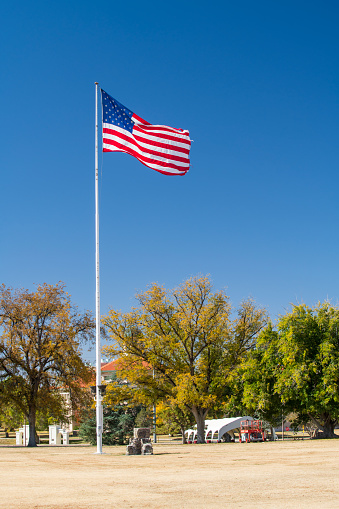 The flag of the United States of America dangling at full-mast on a white pole topped with a golden eagle on ball ornament against deep blue sky.