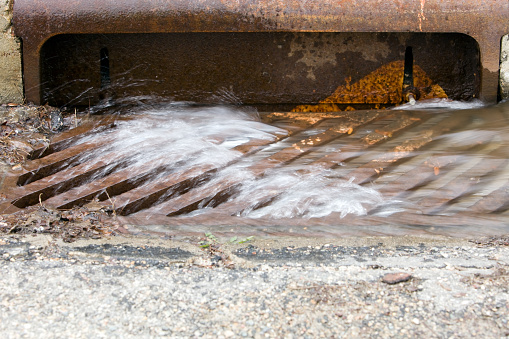 Water is flowing down a residential street's storm drain on an overcast day.
