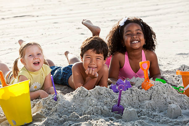 istock Multiracial friends playing in sand at the beach 183871415