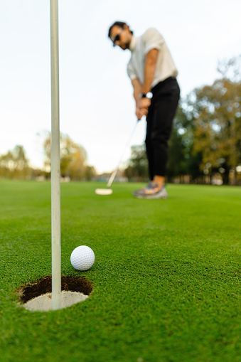 A golfer preparing to strike a golf ball on the golf course on a sunny day - Stock Photo