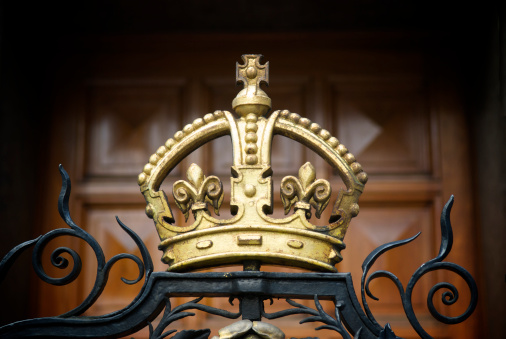 A decorative, gilded crown on a wrought iron fence outside London's National Portrait Gallery with a wood panel door in the background.