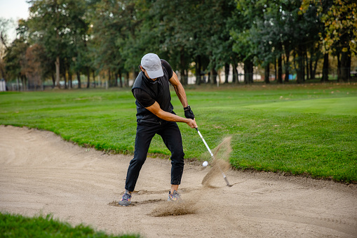 Golfer on the sandy part of the golf course swings the golf club and hits the ball - Stock Photo