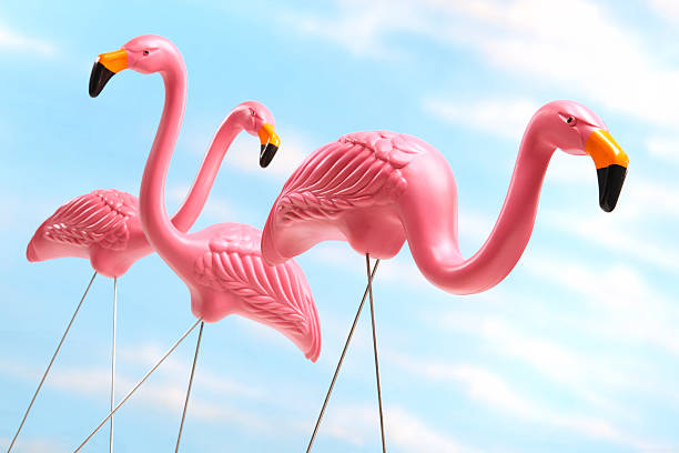 Three pink plastic lawn flamingos against blue sky background Three pink  plastic flamingos stand against a blue sky background.  The kitschy flamingos with wire legs, stand in random directions.  The camera is tilted off axis as a fake sky background mirrors the artificial birds. garden feature stock pictures, royalty-free photos & images