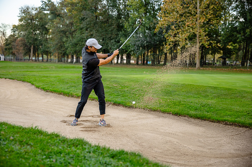 Golfer on the sandy part of the golf course swings the golf club and hits the ball - Stock Photo