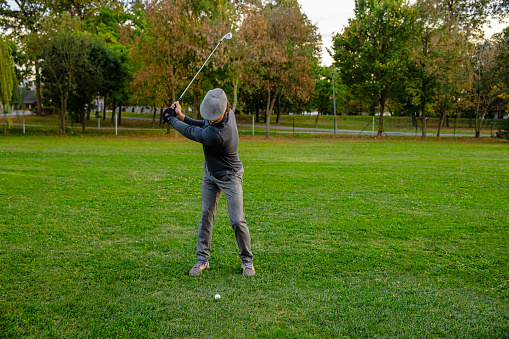 A golfer preparing to strike a golf ball on the golf course on a sunny day - Stock Photo