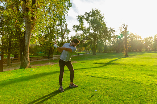 A golfer preparing to strike a golf ball on the golf course on a sunny day - Stock Photo