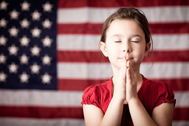 молодая девушка складывать руки и молиться на американский флаг - praying flags стоковые фото и изображения