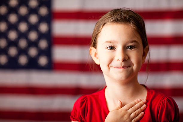 szczęśliwa młoda dziewczyna z ręką na sercu przez amerykańska flaga - child patriotism saluting flag zdjęcia i obrazy z banku zdjęć