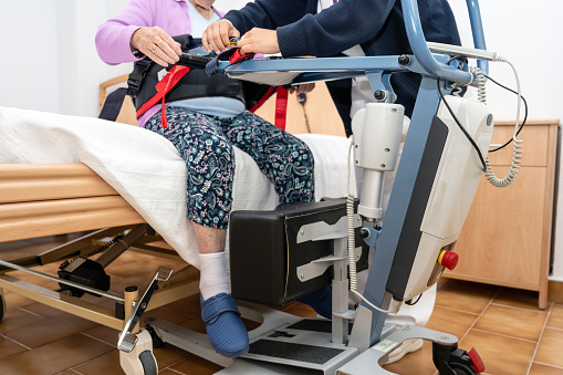 A care staff using a power assist to lifts a patient at nursing home. High quality photography.