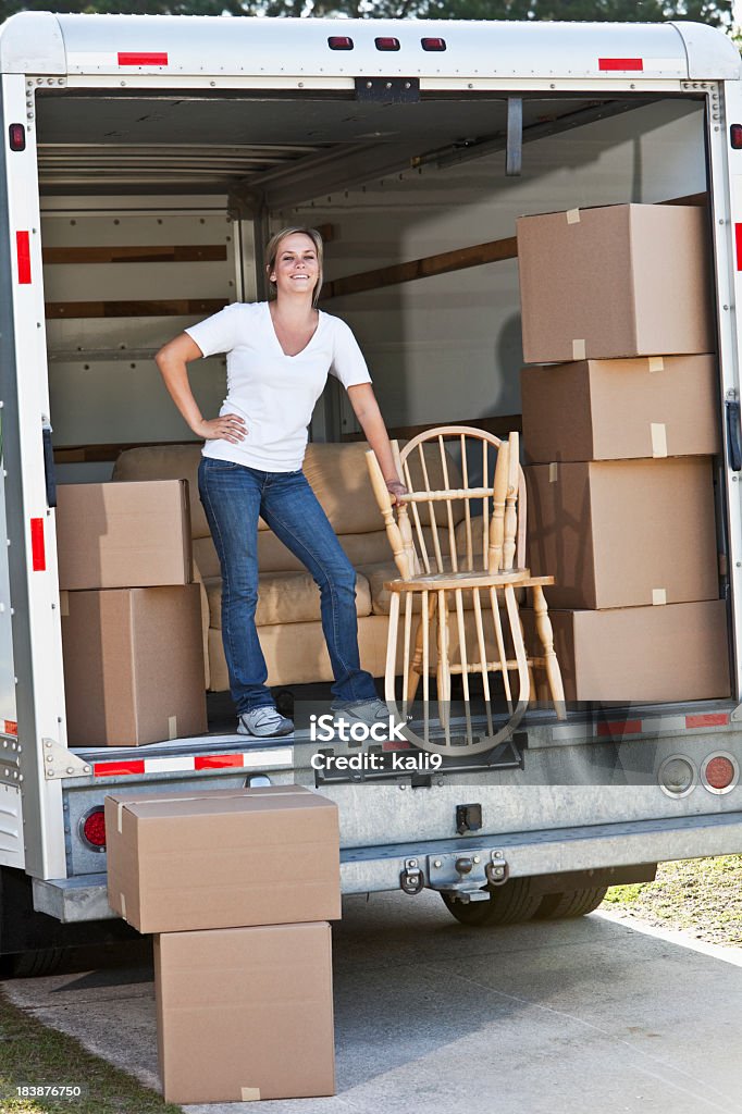 Woman in back of moving van with boxes and furniture Young woman moving house Relocation Stock Photo