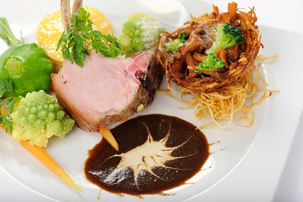 Suckling pig chop with roasted chanterelles in a potato basket and various vegetables.