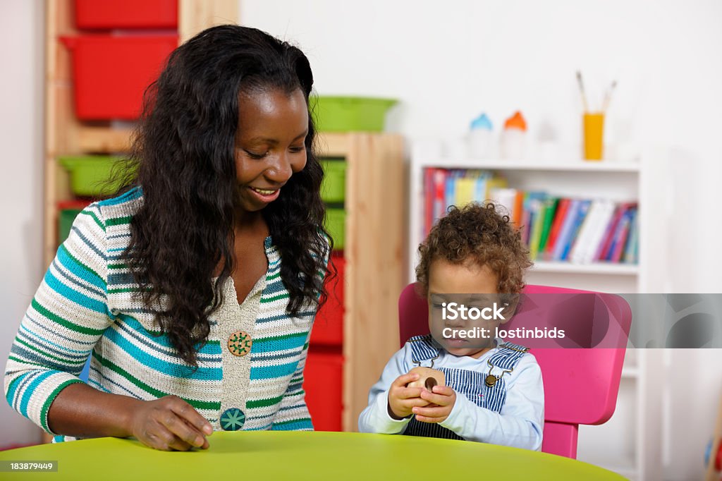Childminder supervisiona bambino piccolo giocando In camera dei bambini - Foto stock royalty-free di 12-17 mesi