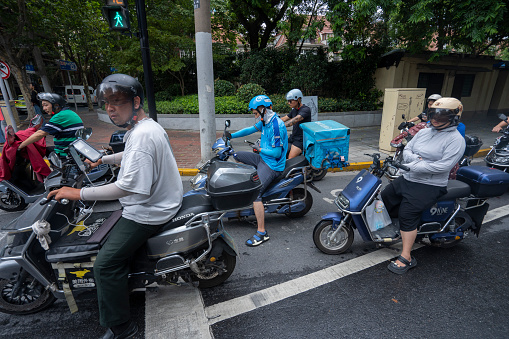 Shanghai, China - Aug 9, 2023: Meituan and Ele.me delivery workers are seen waiting for a green light among other electric bike riders on the streets in Shanghai, China.