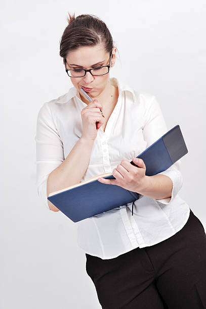 Portrait of  a young businesswoman Portrait of young businesswoman wearing glasses; standind and holding calendar and inkpen. inkpen stock pictures, royalty-free photos & images