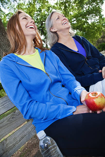 donne ridere insieme con cibo sano su una panchina nel parco - bench sitting tree apple foto e immagini stock