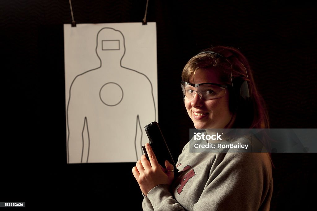 Young Female Shooter - No Bullet Holes "A young woman smiling. Holding a modern polymer, semiautomatic, pistol before shooting her target at the shooting range.  Emphasis on safety as she is wearing ear and eye protection.  No bullet holes, add your own.All images in this series..." Adult Stock Photo