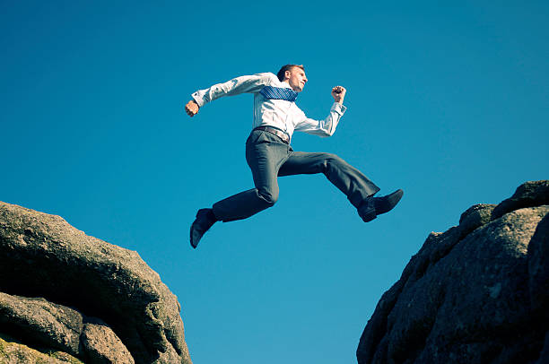 istock Young Confident Businessman Jumping in Blue Sky Between Boulders 183882752