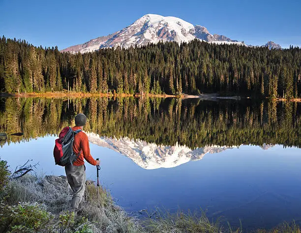 "A hiker by a perfectly still Reflection Lake in Mt. Rainier National Park, Washington State."