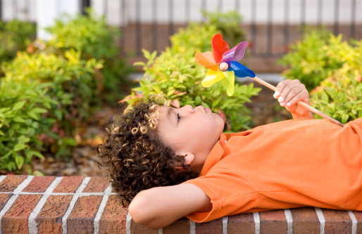 Cute mixed race boy blowing a pinwheel while laying down.