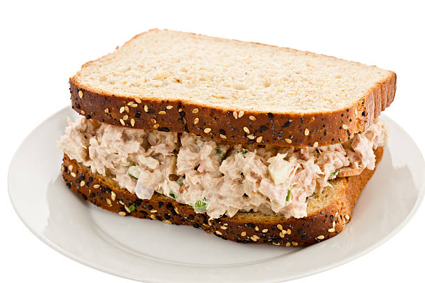 Tuna Salad Sandwich "A close up of a whole tuna salad sandwich consisting of two slices of whole grain bread and tuna salad, on asmall round white plate. Isolated on white." TUNA SANDWICH stock pictures, royalty-free photos & images