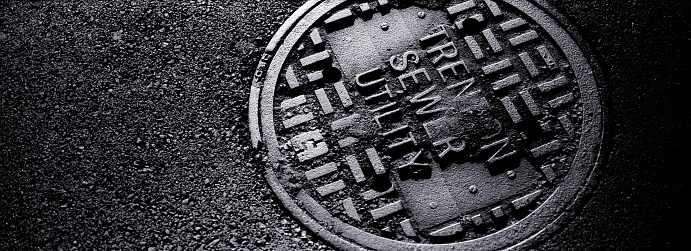 A dark image of a manhole cover in an asphalt street.