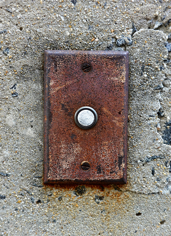 A very rusty old unused button on a concrete wall.