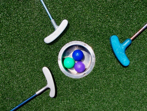 Three colorfull put put miniature golf balls and three putting irons surround a metal hole cup on astroturf for a full frame background. For more sports see my lightbox...