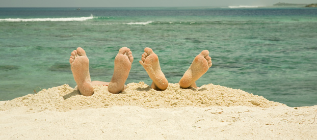 Father and son lying on the beach and you see their sandy feet