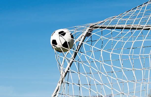 Soccer ball hits the net and makes a goal Soccer ball moves through the air and hits the goal. It's placed perfectly in the upper corner. Blue sky as background. netting stock pictures, royalty-free photos & images