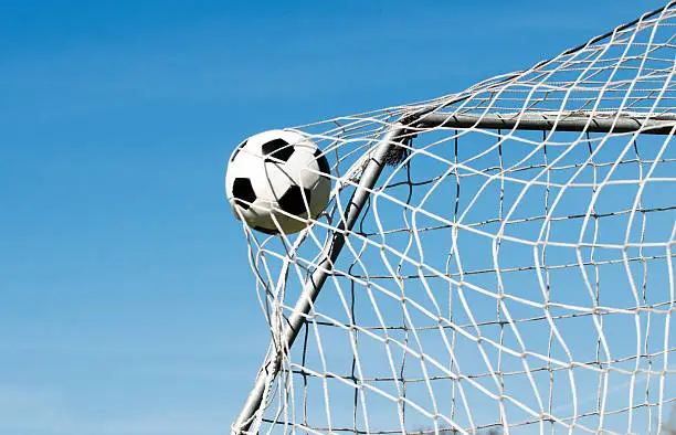 Soccer ball moves through the air and hits the goal. It's placed perfectly in the upper corner. Blue sky as background.