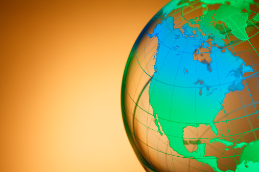A close up of a colorful globe rotated to show North America. The land masses of the globe graduate in color between green and blue against a golden brow background.  Ample copy space exists on left side of image. 