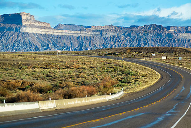 desert road trip "curving road towards desert badlands creates notion of the southwest road trip experience.  taken at the book cliffs, green river, utah.  horizontal composition with selective focus on landscape." sonoran desert desert badlands mesa stock pictures, royalty-free photos & images