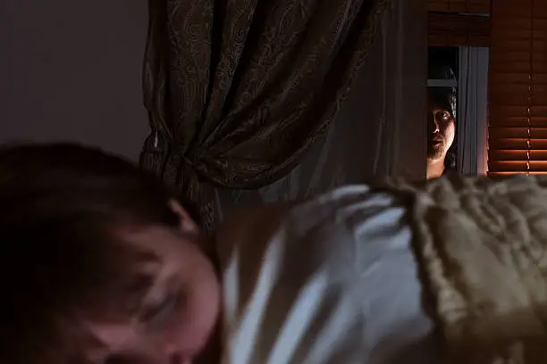 A 38 year old woman (though she doesn't look it) sleeping while a prowler peeks through her bedroom window.