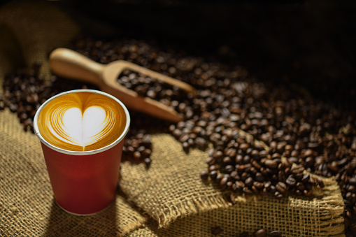 Cup of coffee with heart shape smoke and coffee beans on burlap sack on old wooden background