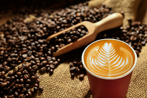 Paper cup of coffee latte and coffee beans on wooden table