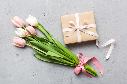 Pink tulips flowers and gift or present box on colored table background. Mothers Day, Birthday, Womens Day, celebration concept. Space for text top view.